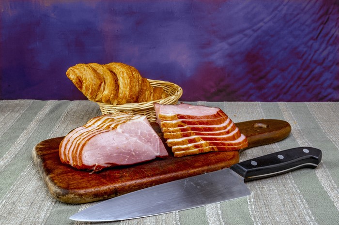 Ham slices and croissant on cutting board with knife