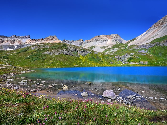 Turquoise lake surrounded by green hills and rocky mountains under a blue sky