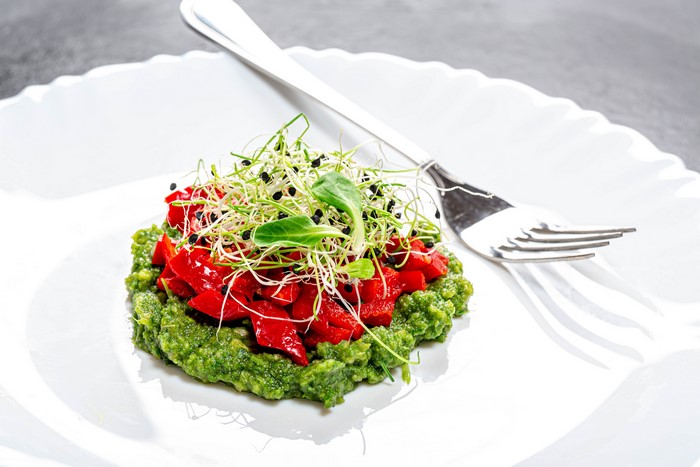 Salad with red peppers and sprouts on a white plate with a fork