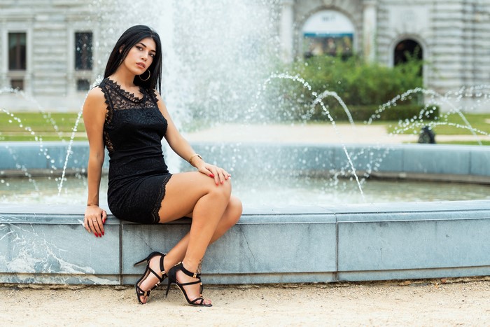 Elegant Brunette Sitting by Fountain in Black Dress