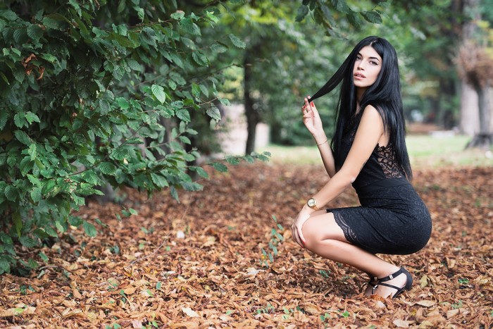 Brunette girl in black dress posing in autumn park