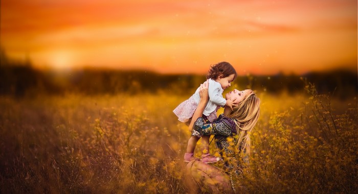 Mother holding daughter in a field at sunset