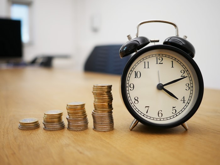 Alarm clock and stacks of coins on a wooden table