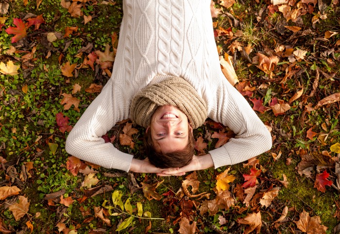 Man lying down in autumn foliage wearing a sweater and scarf