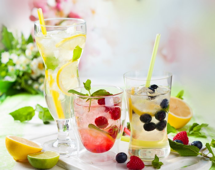 Three refreshing fruit drinks with lemons, limes, raspberries, and blueberries