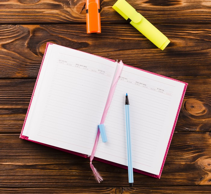 Open notebook with pen and highlighters on wood