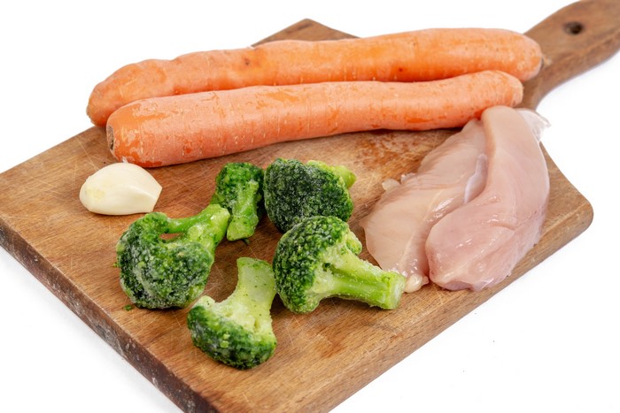 Chicken breast, broccoli, carrots, and garlic on a cutting board
