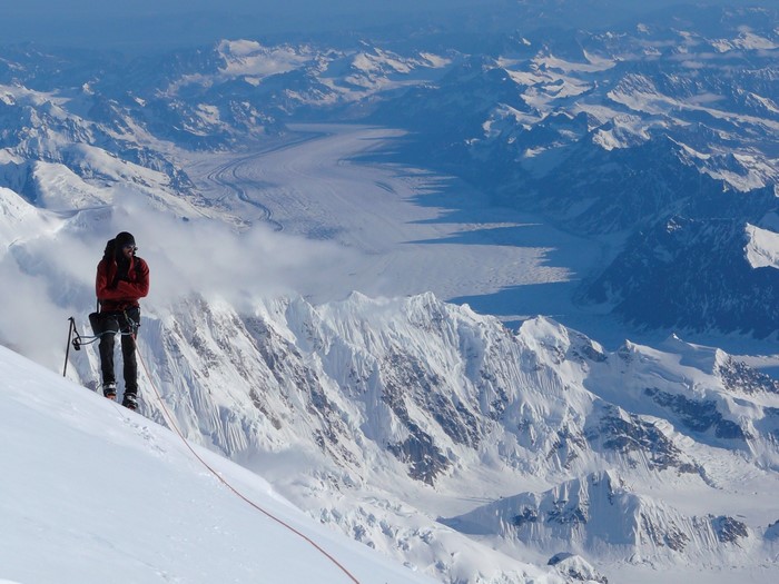 Man mountaineering on a snowy mountain with a glacier in the background