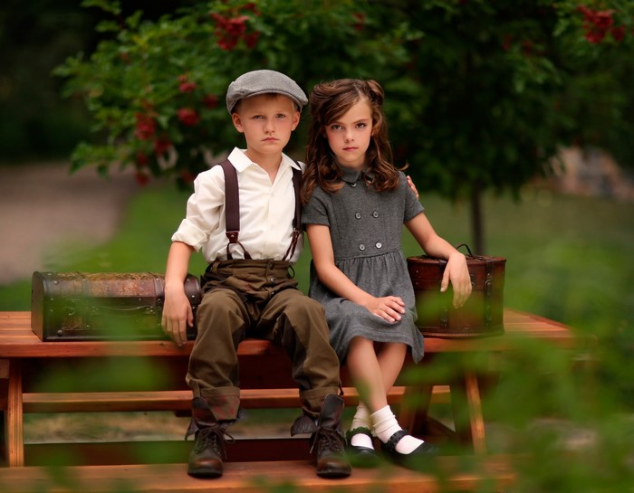 Boy and girl sitting on a bench with vintage luggage