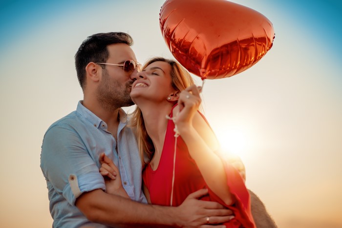 Couple in love with heart balloon at sunset