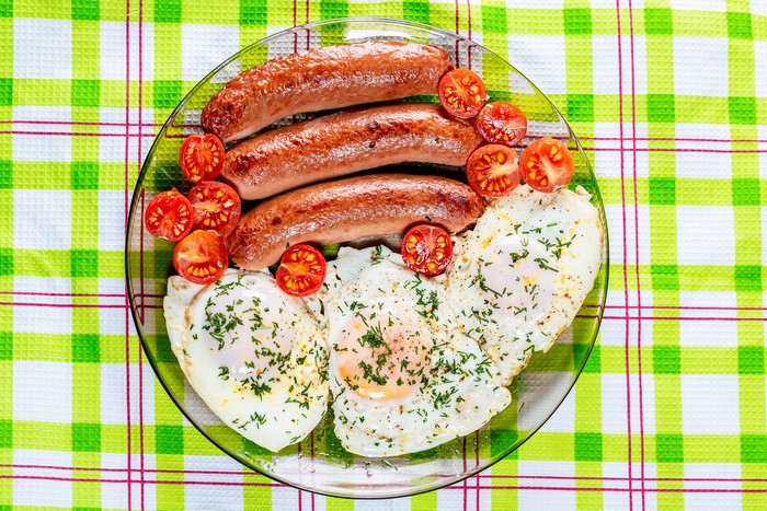 Plate of sausages, fried eggs, and tomatoes with dill
