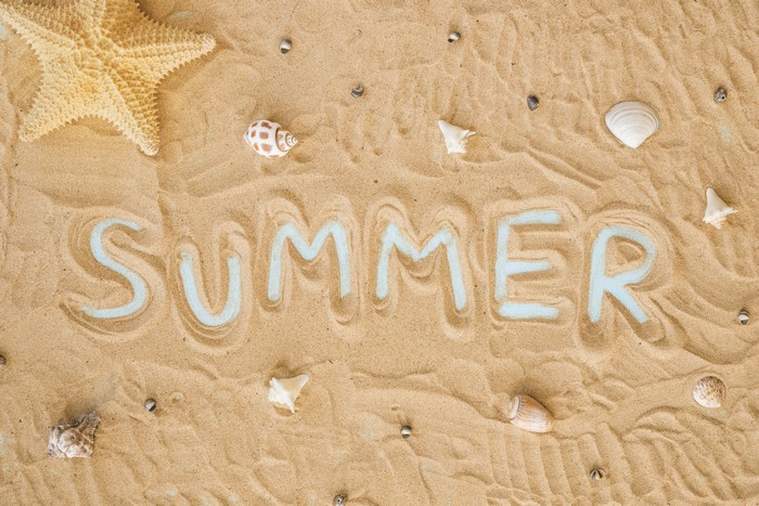 Summer written in sand with starfish and shells
