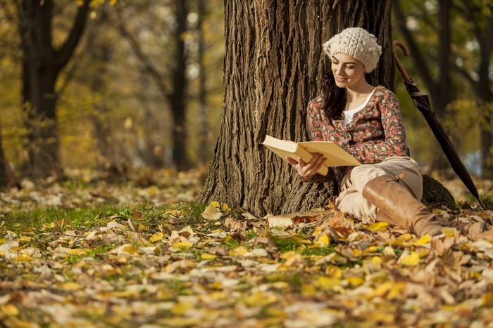Woman reading a book under a tree in autumn