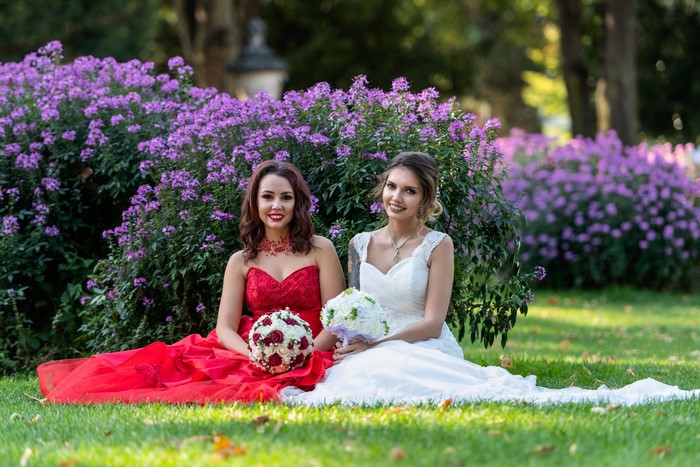 Two women in dresses with bouquets sitting in a garden