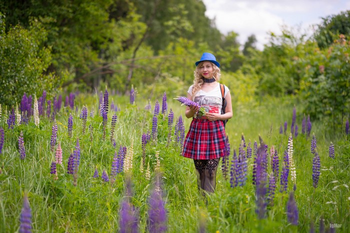 Blonde girl in a hat and skirt in a field of lupines