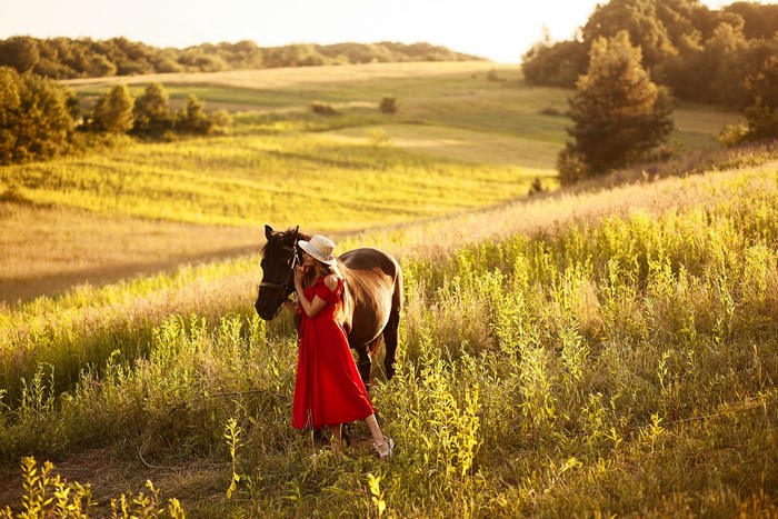 Woman in red dress with horse in a field