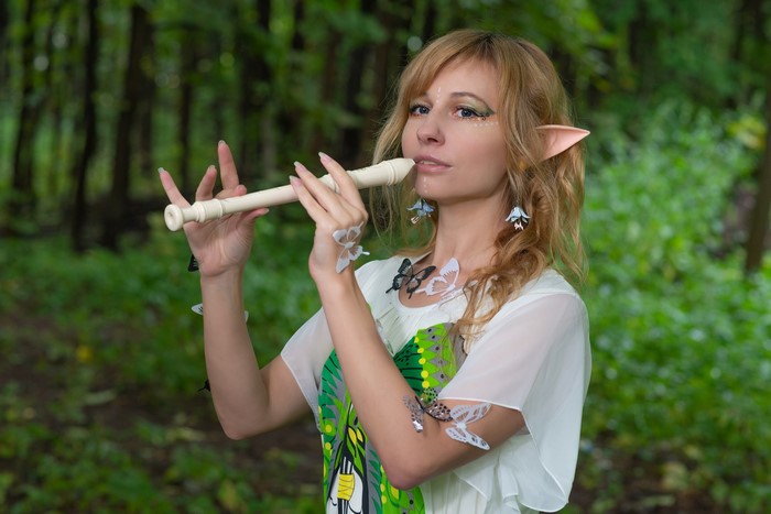 Elf woman playing flute in forest with butterflies