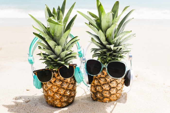 Two pineapples with sunglasses and headphones on a beach