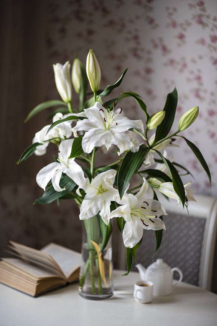 White lilies in a vase with a book and tea set