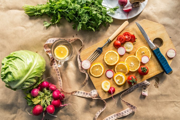 Vegetables, lemons, and radishes on a cutting board with a measuring tape