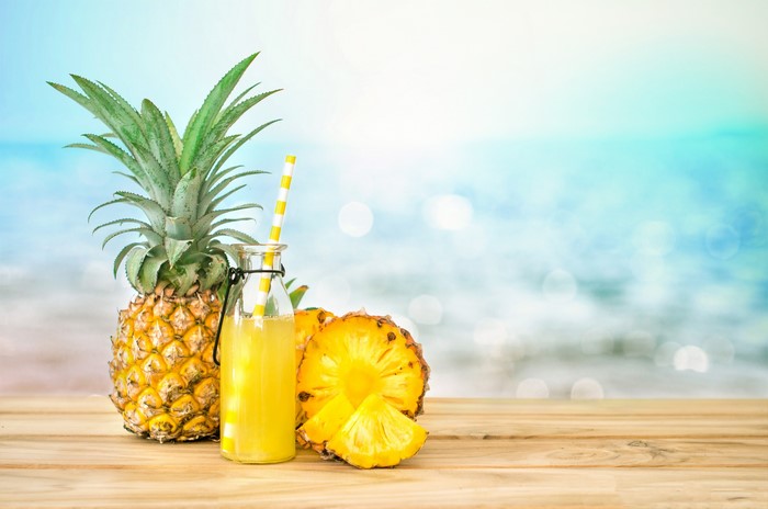 Pineapple juice bottle with pineapples on a beach background