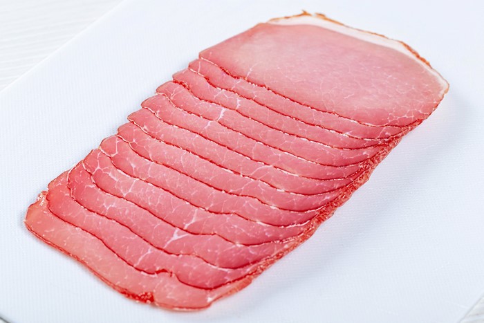 Thinly sliced ham on a white cutting board