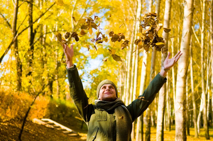 Man throwing leaves in autumn forest