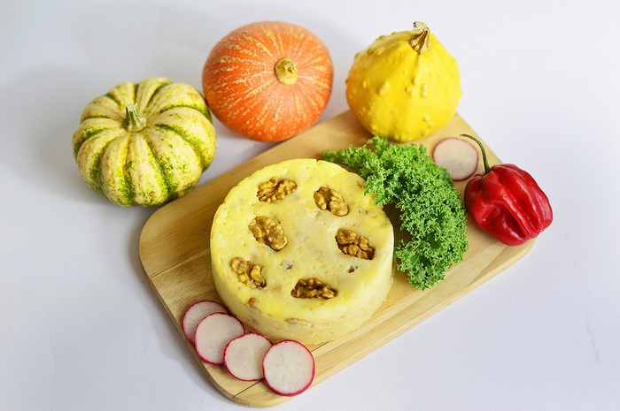 Round pastry with walnuts, pumpkins, bell pepper, and radishes on a cutting board