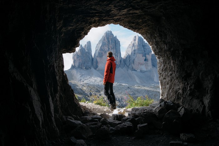 Man in red jacket looking at mountains from cave