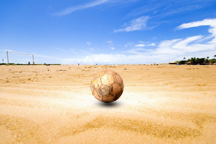 Old soccer ball on a sandy beach with goalposts