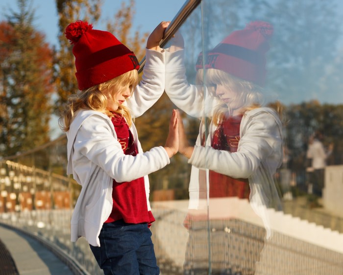 Girl in red hat touching glass reflection