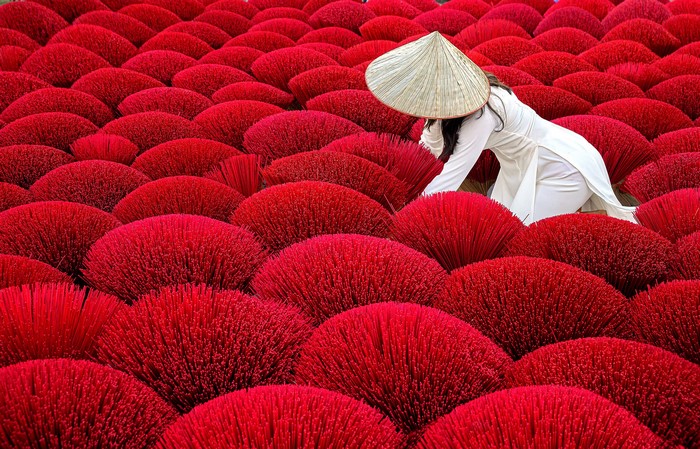 Woman in conical hat among red incense sticks