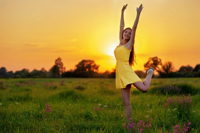 Woman in yellow dress posing in a field at sunset