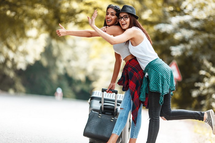 Two young women hitchhiking with a suitcase