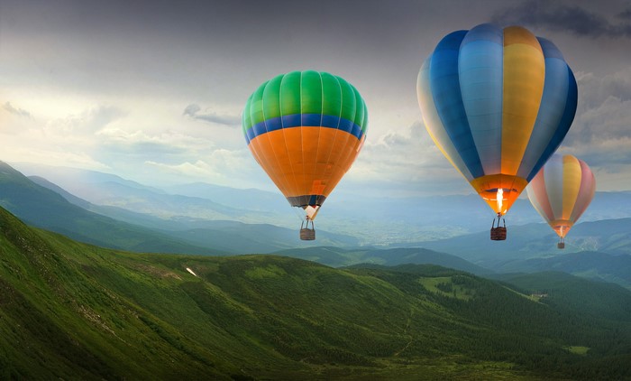 Hot air balloons flying over green hills