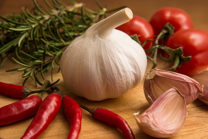 Garlic, chili peppers, tomatoes, and rosemary on a wooden surface