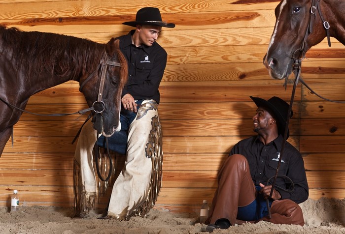 Two cowboys with horses in a stable