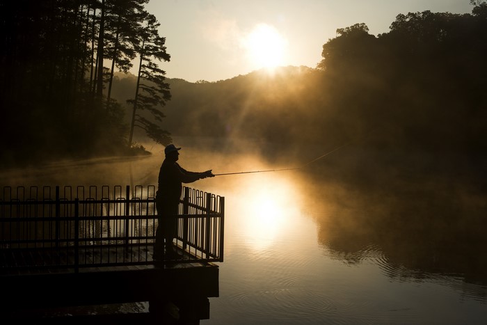Man fishing on a foggy river at sunrise