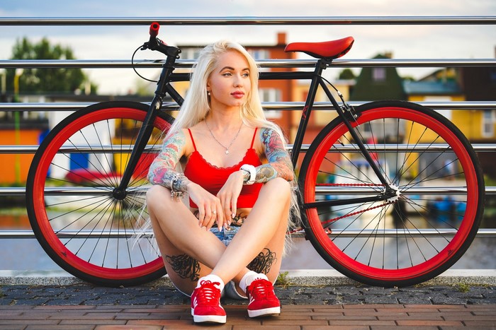 Blonde girl with tattoos sitting by a bicycle