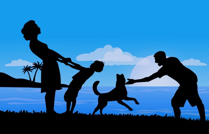 Family playing with dog on beach at sunset