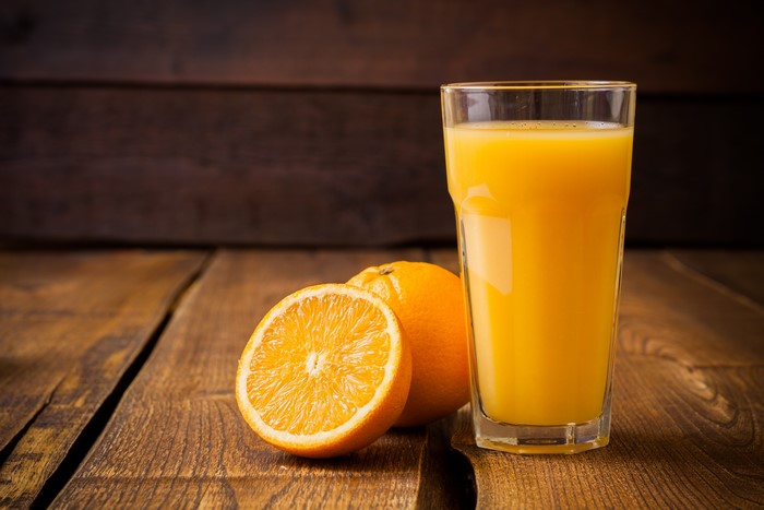 Orange juice in a highball glass with oranges on wood planks