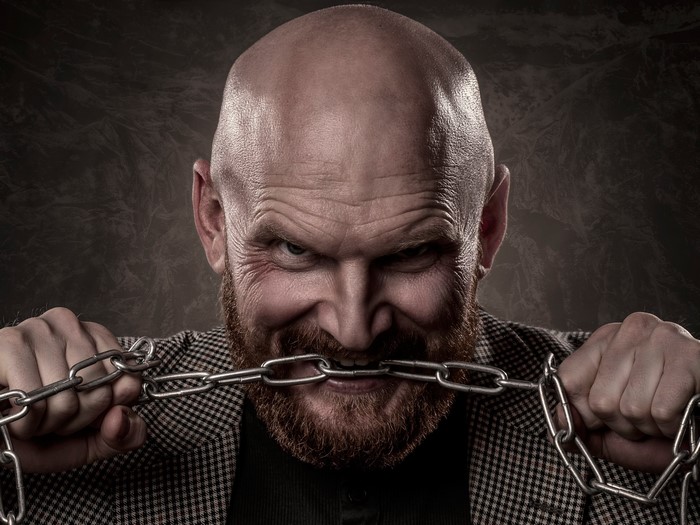 Bald man with beard biting a chain