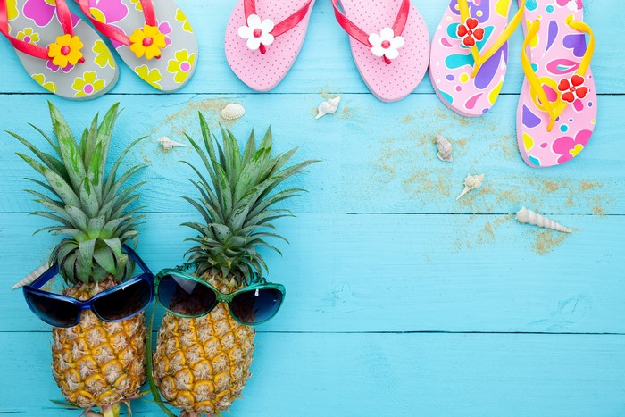 Pineapples with sunglasses and flip-flops on wood