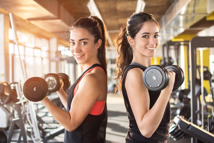 Two women working out with dumbbells in a gym