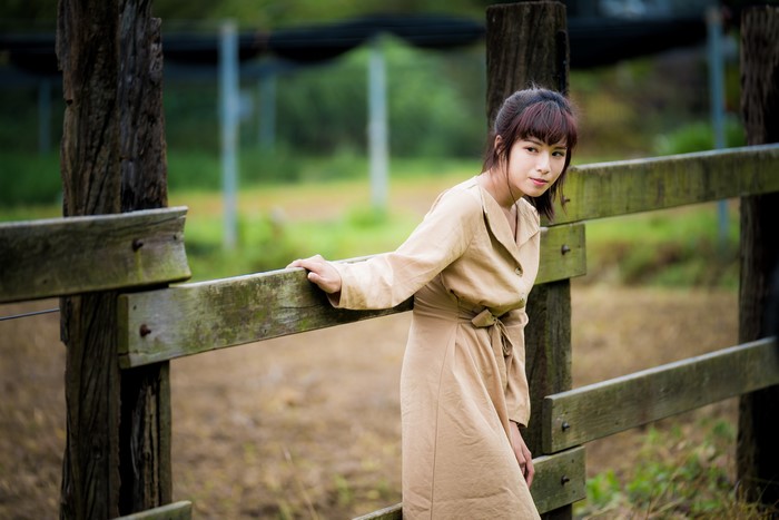 Asian woman in coat posing by a wooden fence
