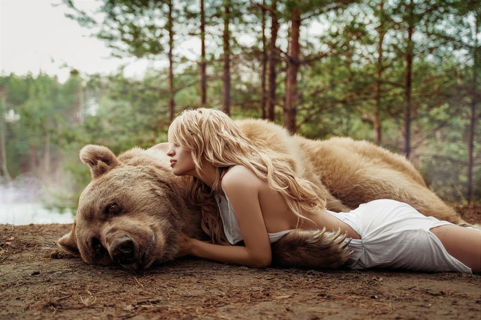 Blonde girl lying with a brown bear in a forest