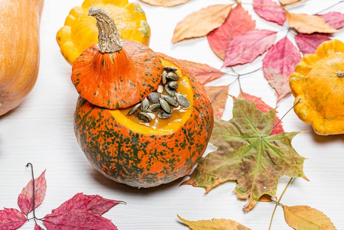 Pumpkin soup served in a pumpkin with autumn leaves