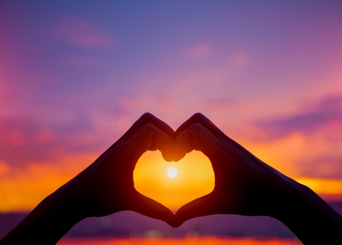 Hands forming a heart shape at sunset