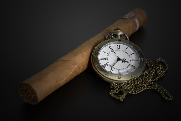 Cigar and pocket watch on a gray background