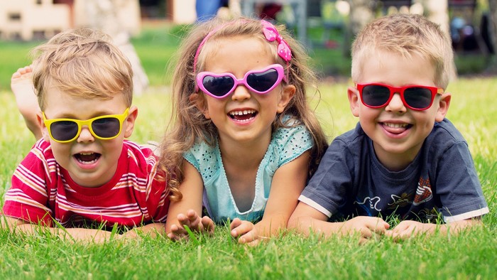 Three children wearing sunglasses lying on grass
